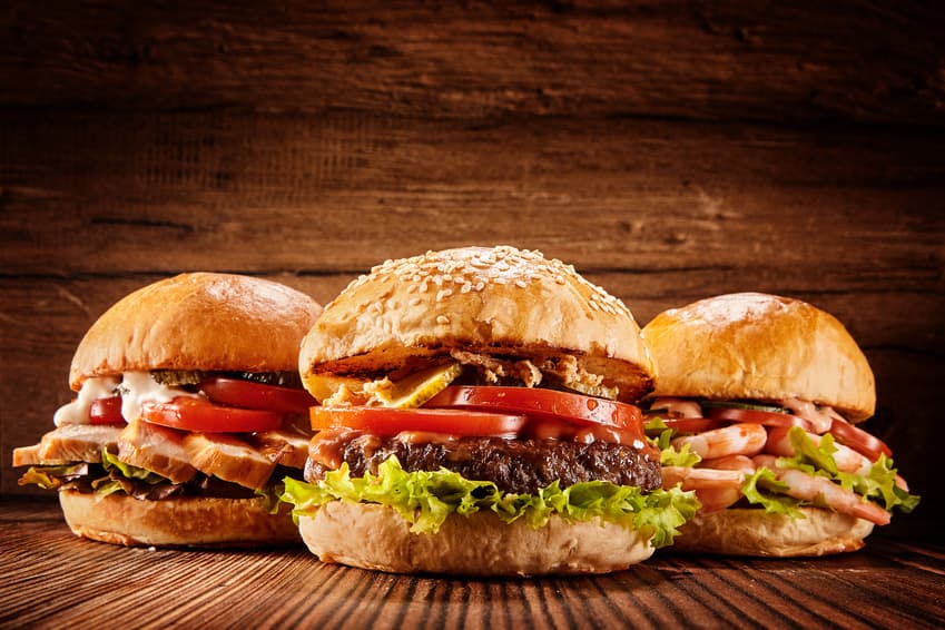 Drei Burger mit Salat und Tomate vor einer Holzwand