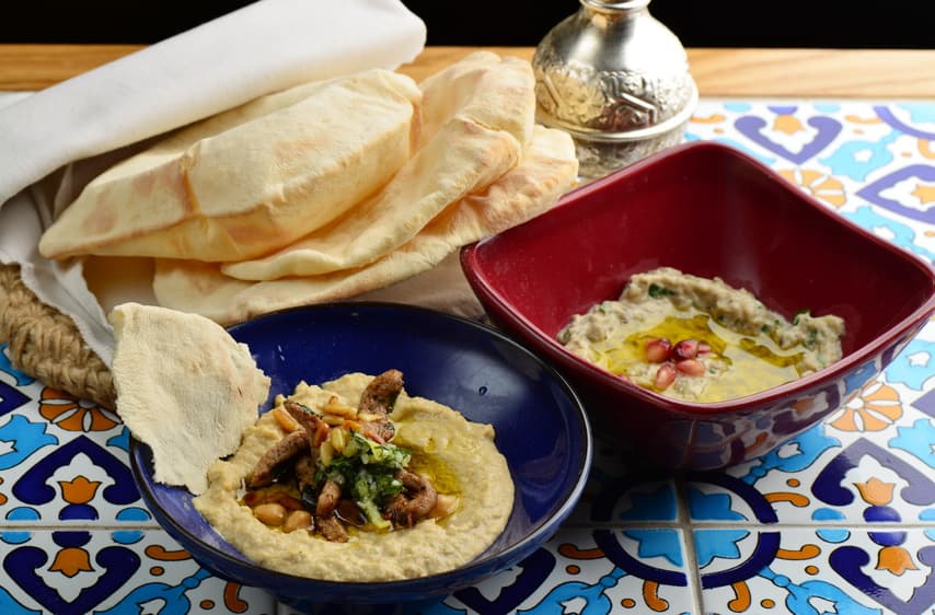 Fladenbrot, Hummus und Auberginenmus in Schalen auf bunten Kacheln