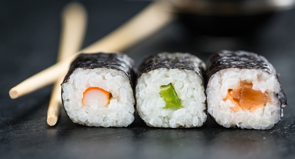 Drei Maki-Röllchen mit Essstäbchen auf dunklem Schiefer