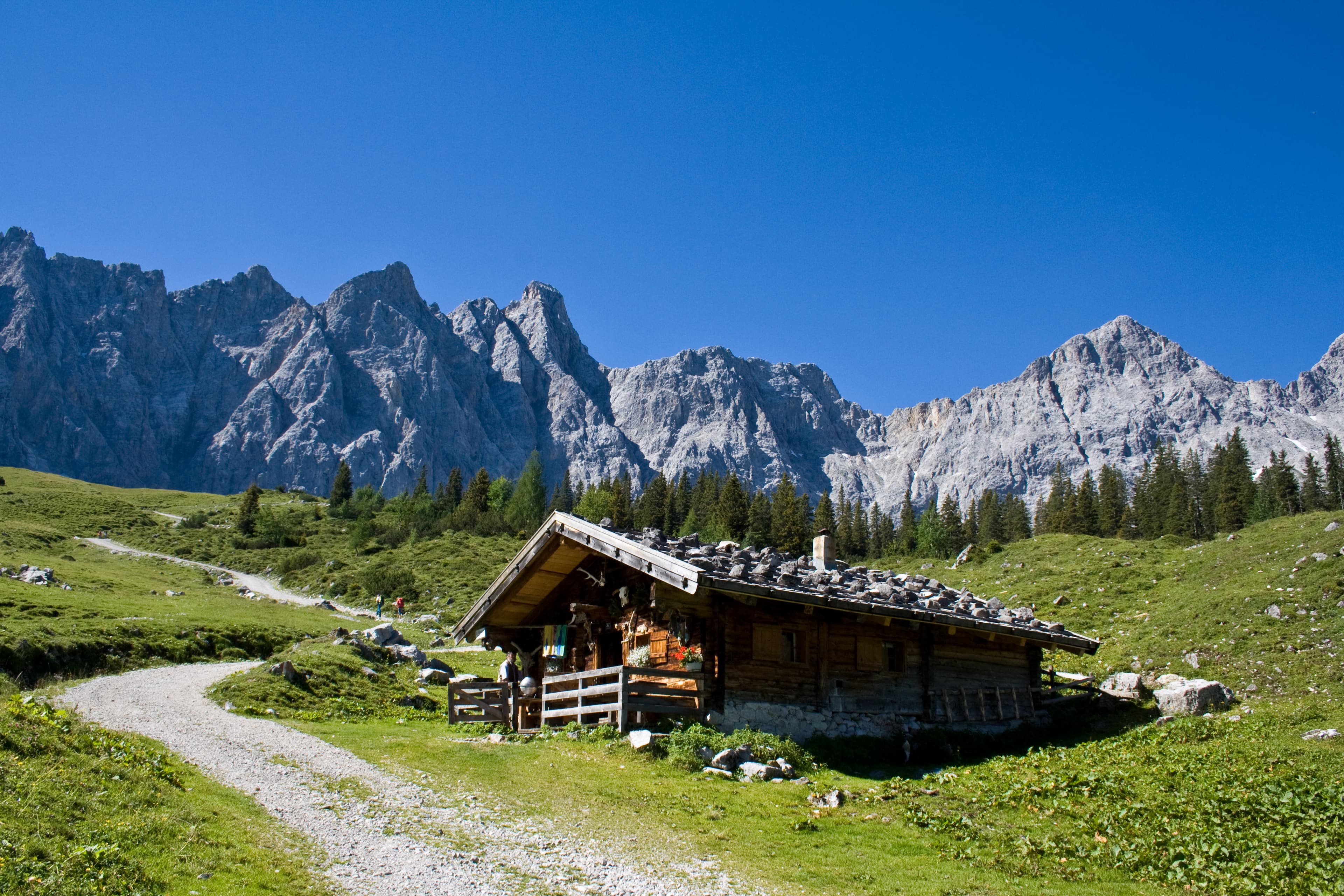 Almhütte vor felsigen Bergen unter blauem Himmel