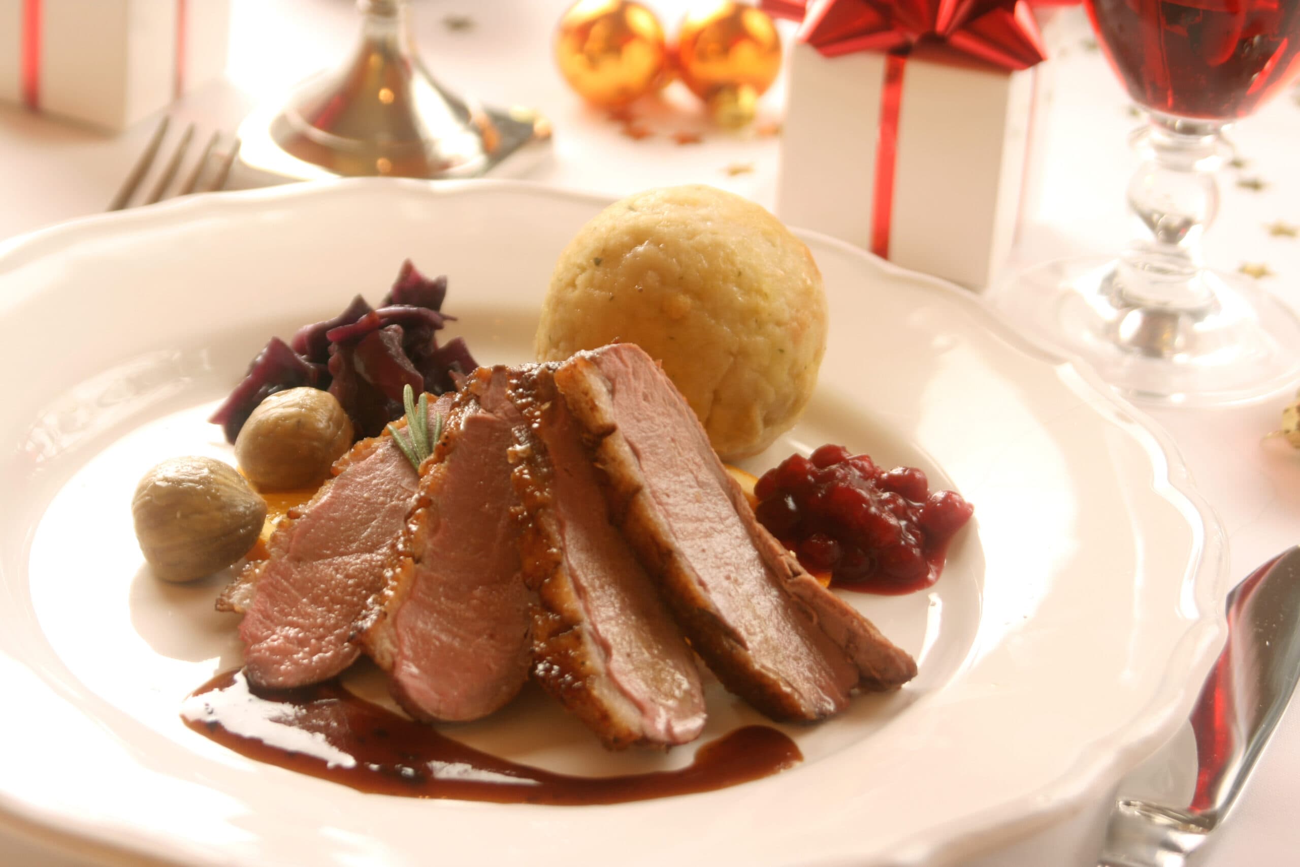 Entenbrust mit Rotkohl, Knödel und Preiselbeeren auf festlich gedecktem Tisch