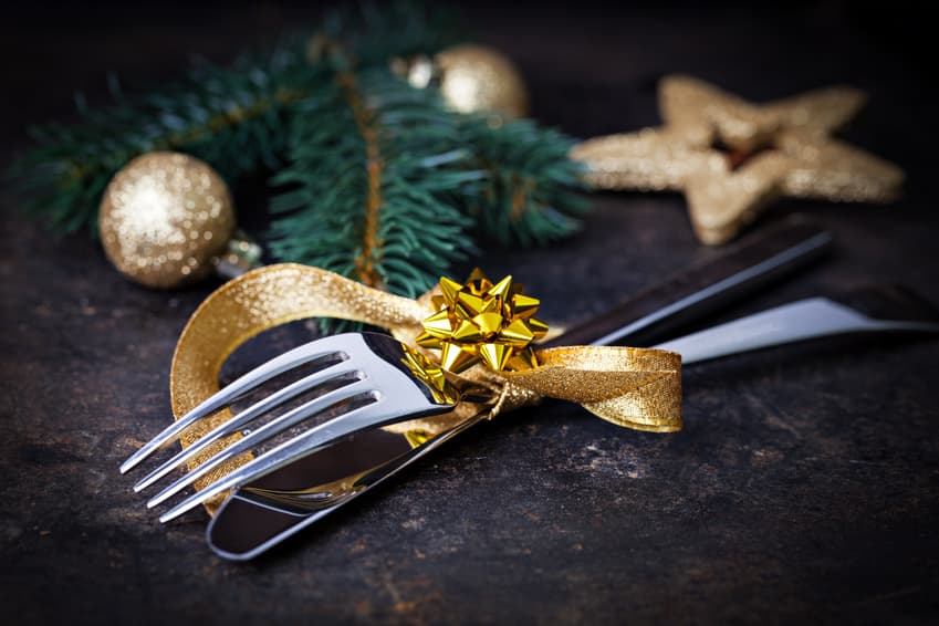 Besteck mit goldener Schleife, Weihnachtskugeln und Tannenzweig auf dunklem Grund