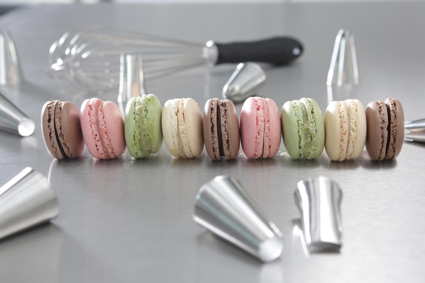 Bunte Macarons in einer Reihe zwischen Spritztüllen und Schneebesen