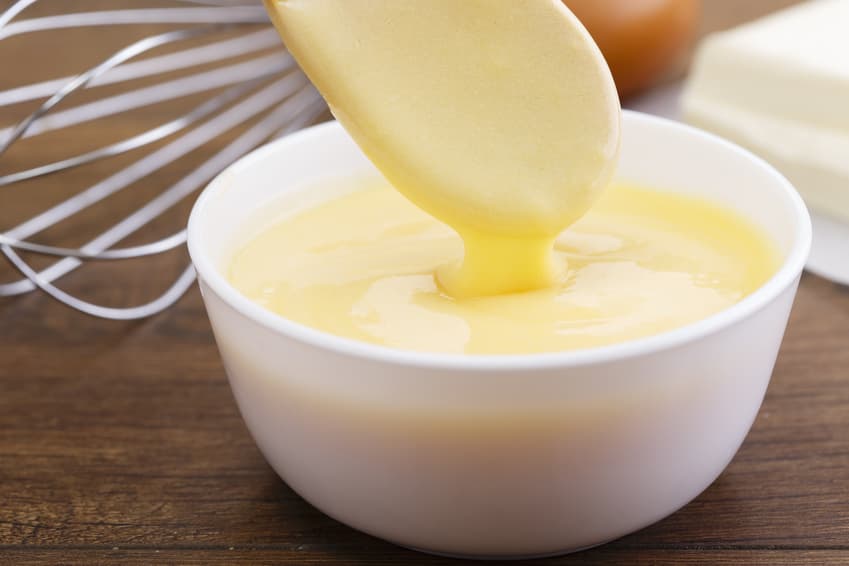 Gelbe Sauce läuft von einem Löffel in eine weiße Schale