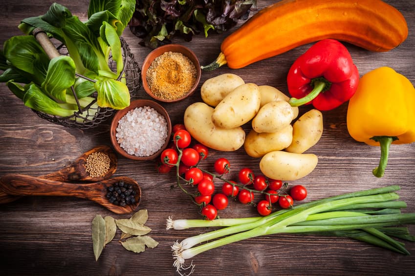 Frisches Gemüse mit Kartoffeln, Tomaten, Paprika und Gewürzen auf dunklem Holz