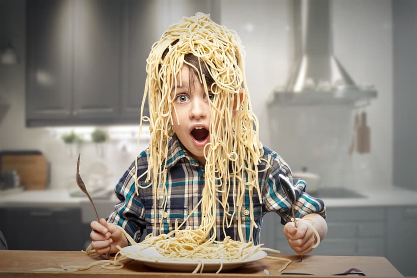 Staunender Junge mit Spaghetti auf dem Kopf in einer Küche