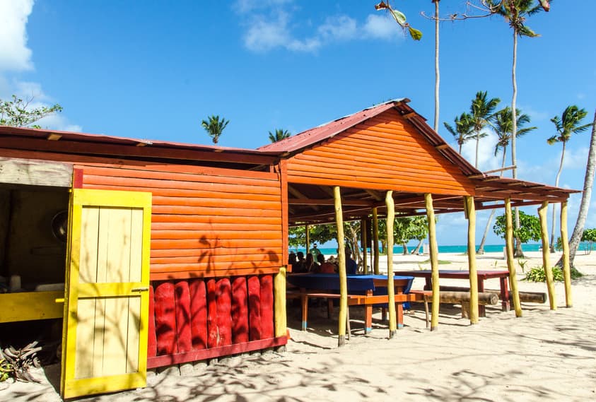 Bunte Strandhütte aus Holz vor Palmen und türkisfarbenem Meer