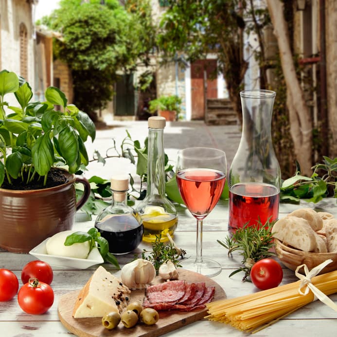 Italienischer Tisch mit Basilikum, Tomaten, Wein, Käse, Salami und Spaghetti