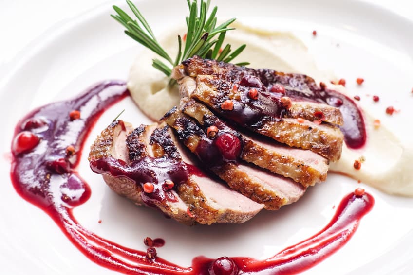 Aufgeschnittene gebratene Entenbrust mit Beerensauce und hellem Püree