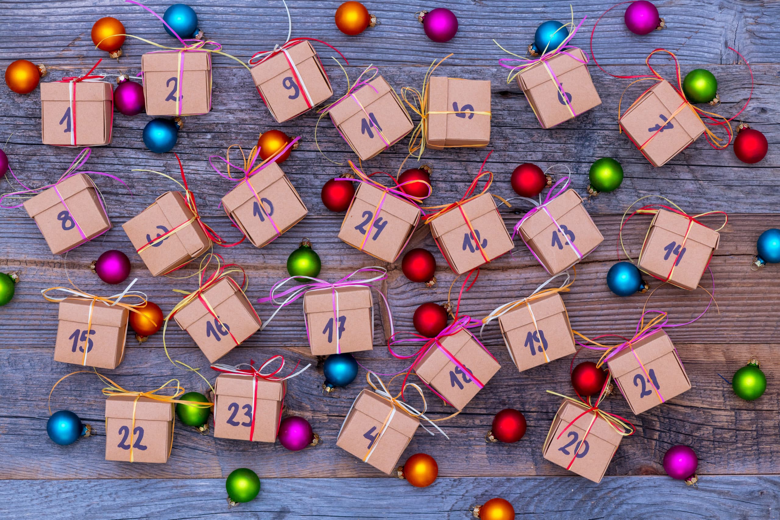 Nummerierte Adventskalender-Päckchen und bunte Christbaumkugeln auf Holz