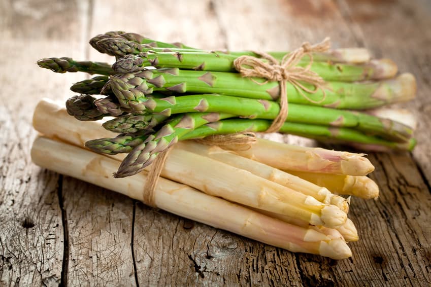 Gebündelter weißer und grüner Spargel auf rustikalem Holz