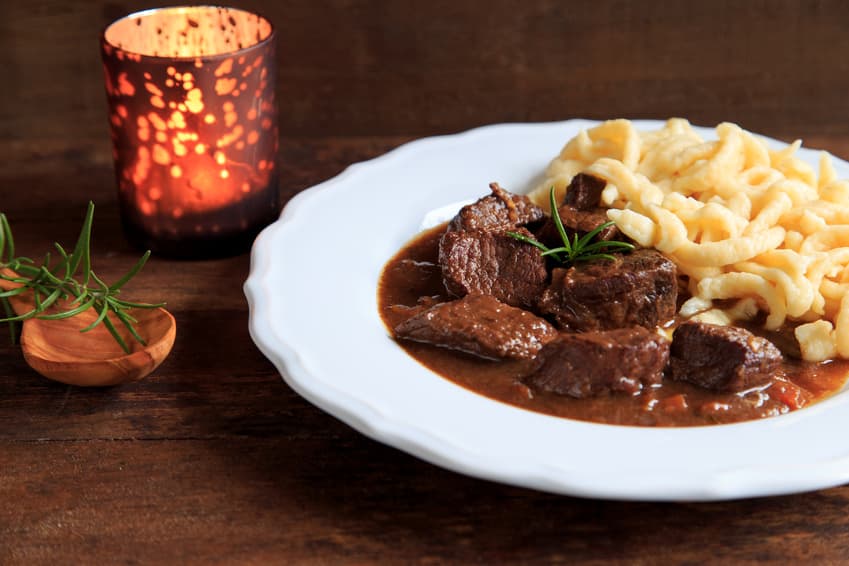 Dunkles Fleischragout mit Spätzle und Rosmarin auf weißem Teller